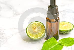 Beautiful packshot of Bergamot essential oil in small glass bottle with fresh bergamot fruit with green leaf on the marble