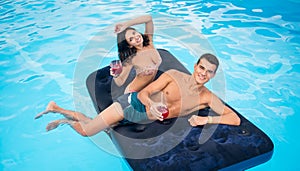 Beautiful pair floating on mattress in swimming pool, drinking cocktails and having fun on their summer vacation