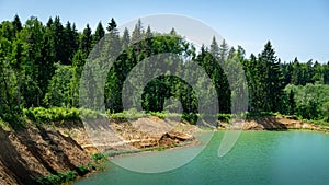 Beautiful panorama of quarry lake with emerald green water and big forest as background. Closed down quarry now