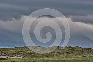 Beautiful panoramic landscape on Dingle Peninsula, Ireland. Panoramic dune landscape with mountain silhouettes and dark rain