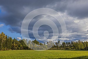 Beautiful panoramic view of autumn landscape with forest colorful trees and green field on background of blue sky with clouds.