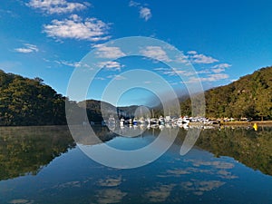 Beautiful panoramic view of creek with reflections boats, blue sky, light clouds, fog, mountains and trees on water
