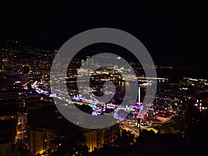 Beautiful panoramic view of the illuminated downtown of Monaco at night with funfair and marina Port Hercule.