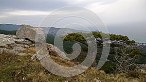 Beautiful panoramic view of the lonely tree on the hill and large stone boulders. The view down the mountain in cloudy weather
