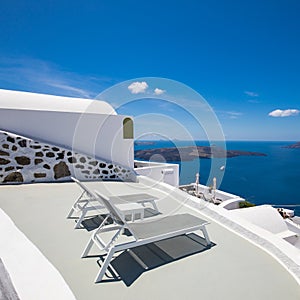 Luxury travel destination in Santioni island, Greece. White houses and caldera sea view with loungers under blue sky, romance