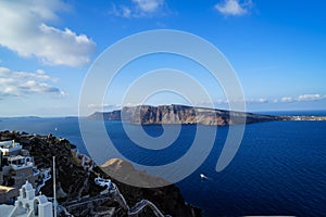 Beautiful panoramic view of vast blue Aegean sea, sailing ships and natural caldera mountain from Oia village with white buildings