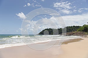 Beautiful paradise beach with big rocks on a sunny day with blue sky with white clouds, waves in the sea and some sunbathers