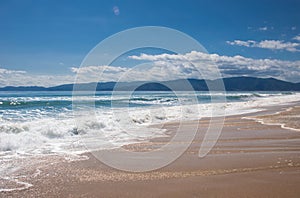 Beautiful paradise sandy beach, sea waves, foam, blue sky, white clouds.