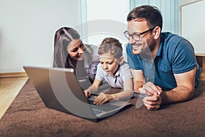 Parents and their son are doing shopping online using laptop and smiling at home