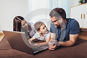 Parents and their son are doing shopping online using laptop and smiling at home