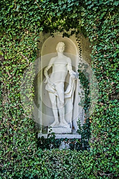 Beautiful park hedge with white ancient roman statue of man. Lush Green Topiary