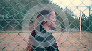 Beautiful and passionate girl in a biker jacket behind an iron fence. Young woman behind bars locked metal fence.