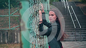 Beautiful and passionate girl in a biker jacket behind an iron fence. Young woman behind bars locked metal fence.