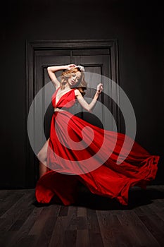 Beautiful and passionate woman in the red evening fluttering dress is capture in move, the wooden door is on the background