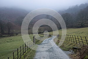 Beautiful peaceful Winter landscape image of road around Loughtrigg Tarn on misty morning with calm water and foggy countryside in