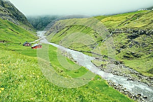 Beautiful peaceful wooden house in Saksun valley with green grass next to the river in foggy weather, Faroe Islands, North Europe