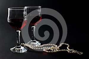 Beautiful Pearl Necklace and Two Glass Cups of Red Wine Isolated on Black