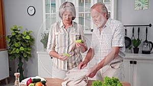 beautiful pensioners follow healthy lifestyle and take out fresh healthy vegetables from eco bags on kitchen table at