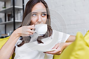 beautiful pensive brunette girl drinking coffee and looking away