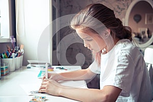 Beautiful pensive teenager girl drawing sketch at her table with light from window in home