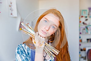 Beautiful pensive young woman painter holding paintbrushes in art studio