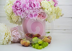 Beautiful peonies in the pink box with fruits on wooden background