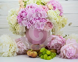 Beautiful peonies in the pink box with fruits on wooden background