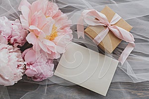 Beautiful peony bouquet, gift and card on soft tulle  on dark wood, top view. Happy Mothers day