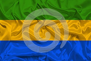 Beautiful photo of the national flag of Gabon on delicate shiny silk with soft draperies, the concept of state power, country life