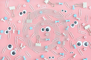 Photo with scattered stationery. Funny faces with puppet eyes. Clips, clerical buttons and asterisks in a mess on a pale