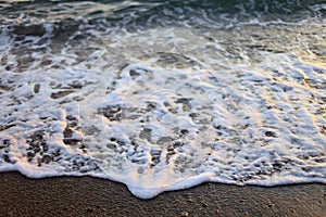 A beautiful picture of a sea wave with foam running onto the beach in the rays of the setting sun. Sea waves at sunset