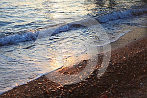 A beautiful picture of a sea wave with foam running onto the beach in the rays of the setting sun. Sea waves at sunset