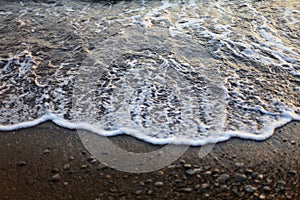 A beautiful picture of a sea wave with foam running onto the beach in the rays of the setting sun. Sea waves at sunset