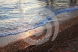 A beautiful picture of a sea wave with foam running onto the beach in the rays of the setting sun. Sea waves at sunset