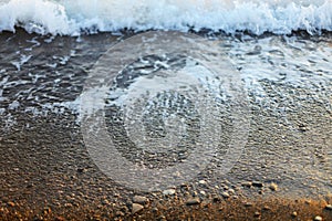 A beautiful picture of a sea wave with foam running onto the beach in the rays of the setting sun. Sea waves at sunset