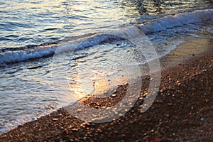 A beautiful picture of a sea wave with foam running onto the beach in the rays of the setting sun. Sea waves at sunset