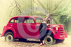 Beautiful pin-up girl in jeans and a plaid shirt is leaning on a red retro car. Retro style.