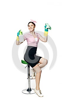 Beautiful pin-up girl in a pink shirt with rubber gloves for cleaning holds a rag and spray for washing windows and looks with a w