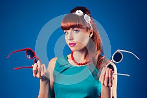 beautiful pin-up girl posing with two pairs of sunglasses against blue background