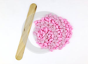 Beautiful pink depilatory wax granules and wooden spatulas on a white background.