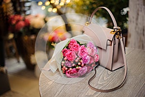 Beautiful pink flowers near the stylish handbag on the table