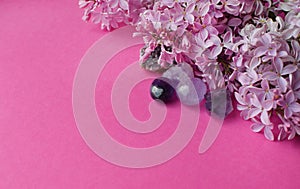 Beautiful pink lilac flowers and semi-precious stones, rose quartz and amethyst lie on a pink background. Copy space