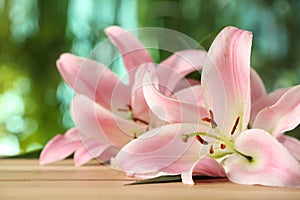Beautiful pink lily flowers on wooden table against blurred green background, closeup