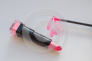 beautiful pink lip gloss smear with brush and a tube of lipstick, white background