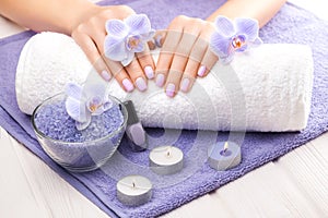 Beautiful pink manicure with orchid, candle and towel on the white wooden table.