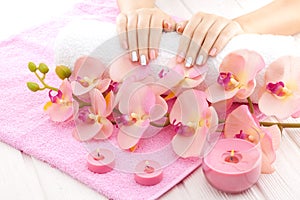 Beautiful pink manicure with orchid, candle and towel on the white wooden table.