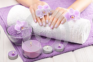 Beautiful pink manicure with orchid, candle and towel on the white wooden table.