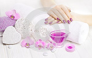Beautiful pink manicure with orchid and towel on the white wooden table. spa