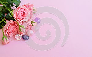 Beautiful pink rose flowers in full bloom with green leaves. Bouquet of flowers on a pink background with amethysts, rose quartz