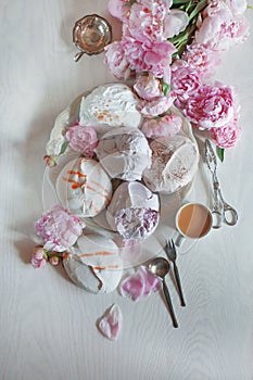 Beautiful pink, rose peonies decorated with tasty meringues on white wood table